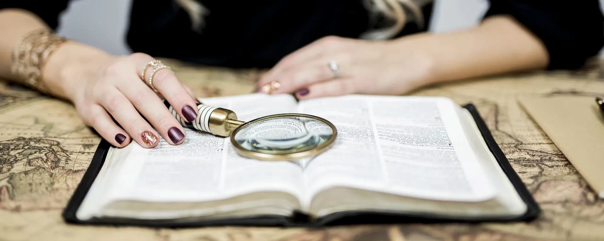 Close up de una persona con una lupa investigando un libro.